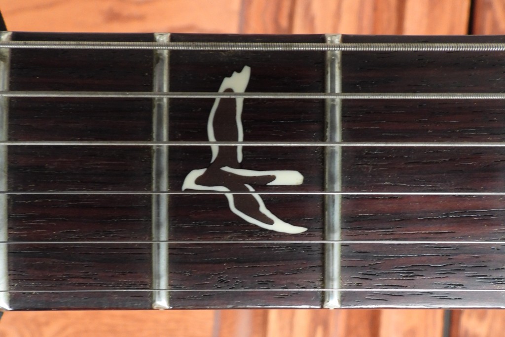 Close-up of dark (rosewood) guitar fretboard with white, harrier-shaped inlay.